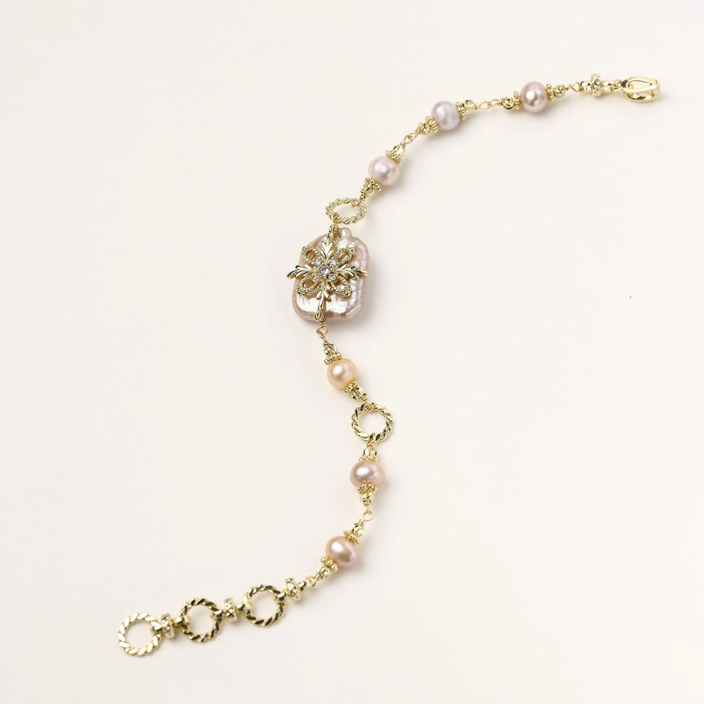 Gold-plated chain bracelet with baroque pearl centerpiece and floral charm, featuring mixed freshwater pearls.