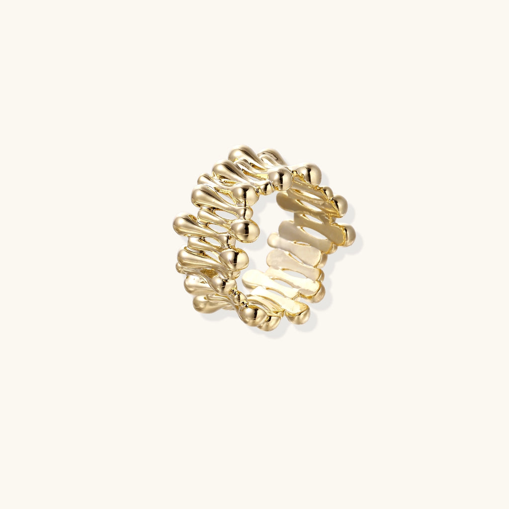 Close-up of chunky 18K gold-plated brass ring with flowing wave-like sculptural design on neutral background.