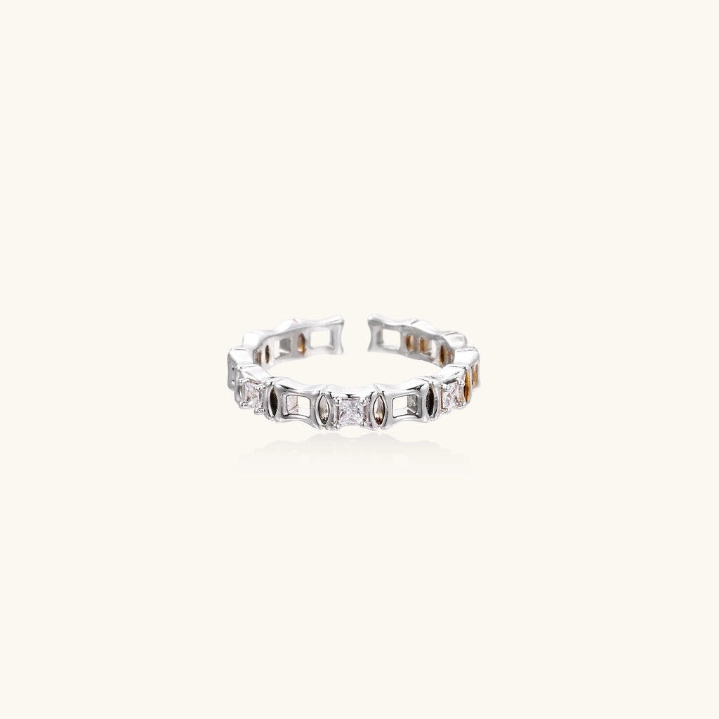 Close-up of geometric gold-plated ring with alternating rectangular blocks and zirconia crystals on white background.