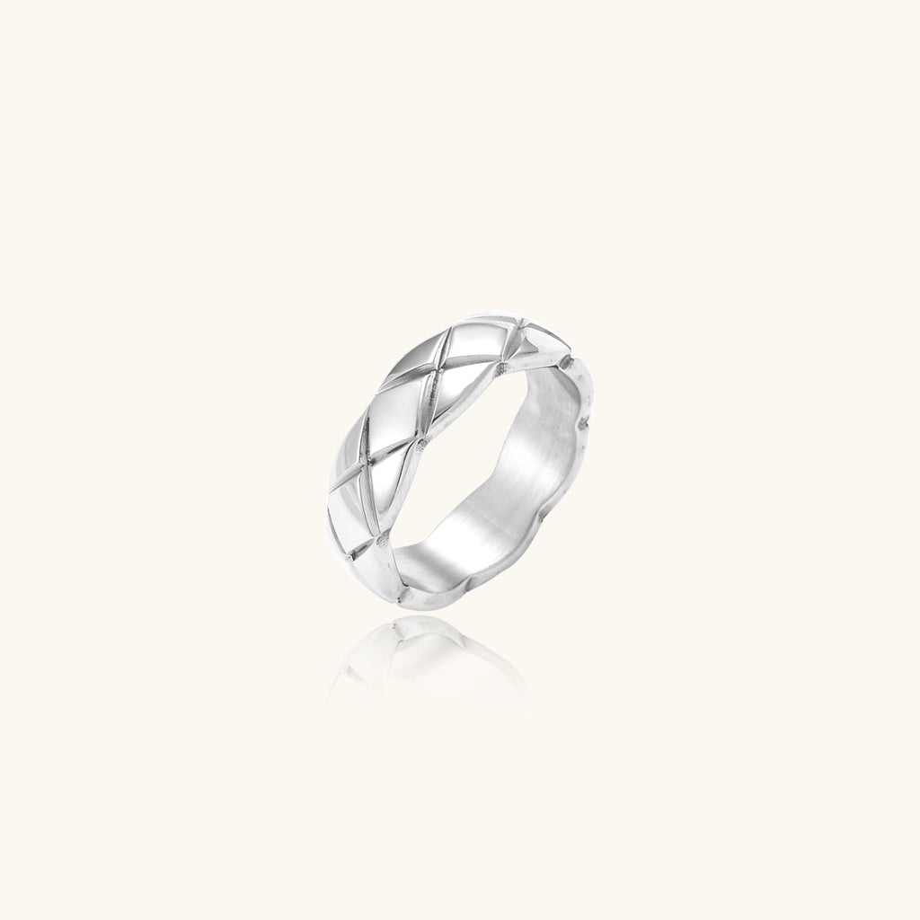 Close-up of a polished stainless steel ring featuring a geometric quilted diamond pattern on white background.