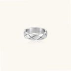 Close-up of a polished stainless steel ring featuring a geometric quilted diamond pattern on white background.